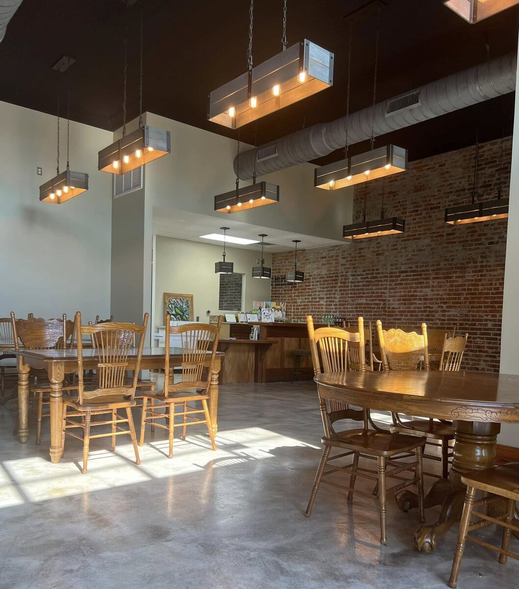 Inside The Russo looking toward the wooden service bar at the back, with vintage tables and chairs, exposed brick, and warm pendant lighting.