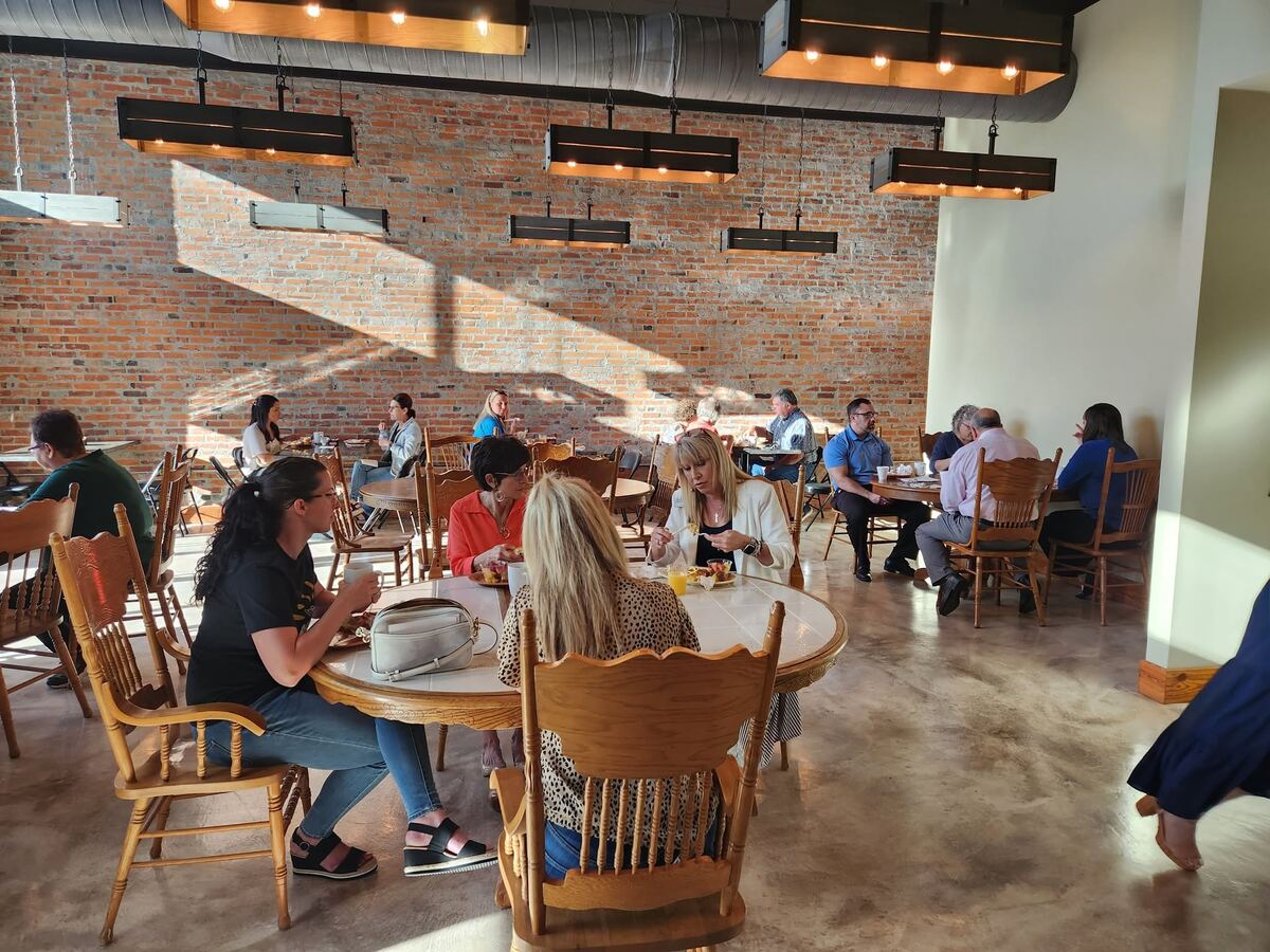 Guests enjoying a luncheon at round tables inside The Russo, sunlight across the exposed brick wall.