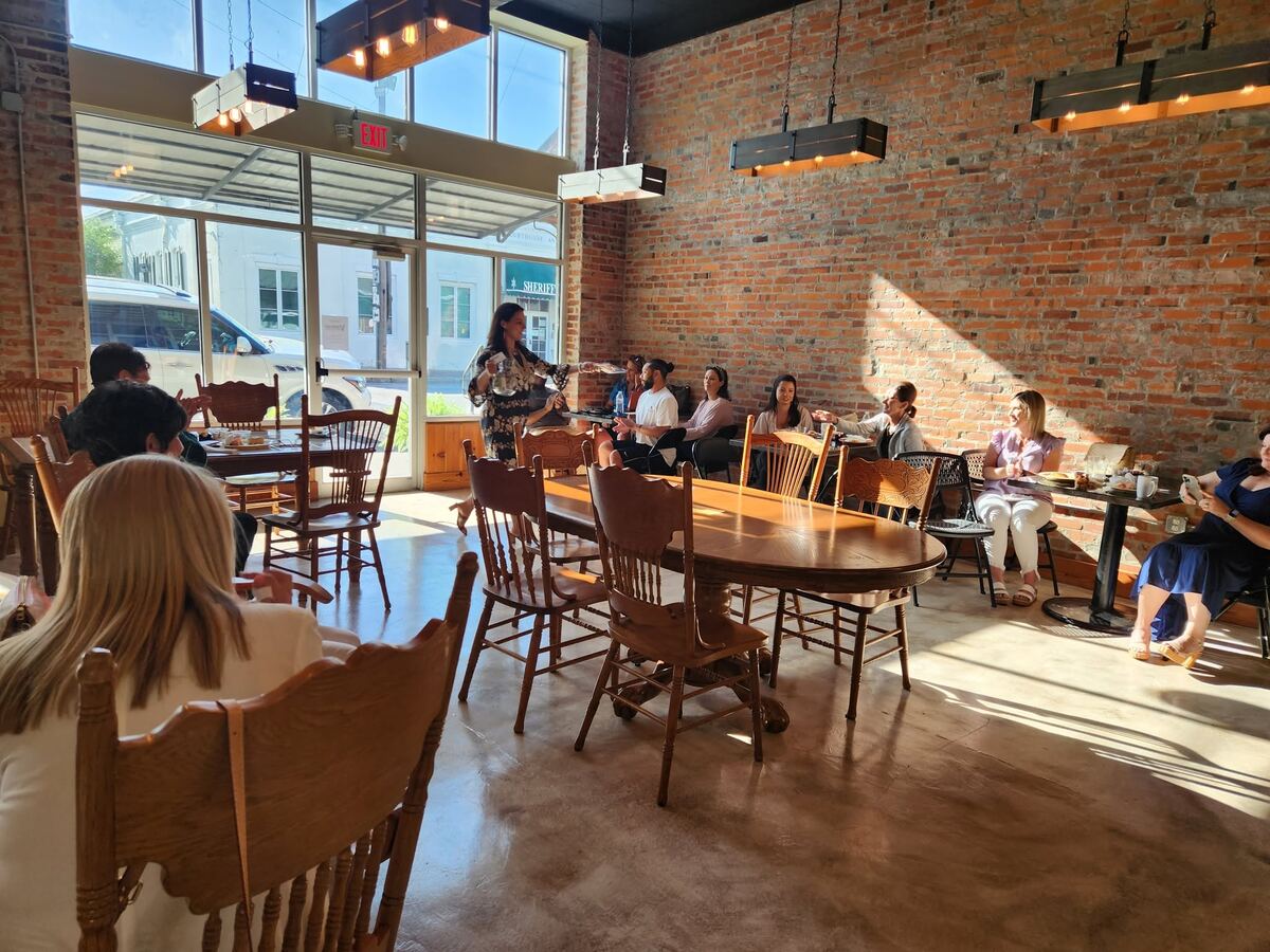 A host presenting to a seated group at The Russo, guests gathered around tables in the sunlit brick room for a workshop-style event.