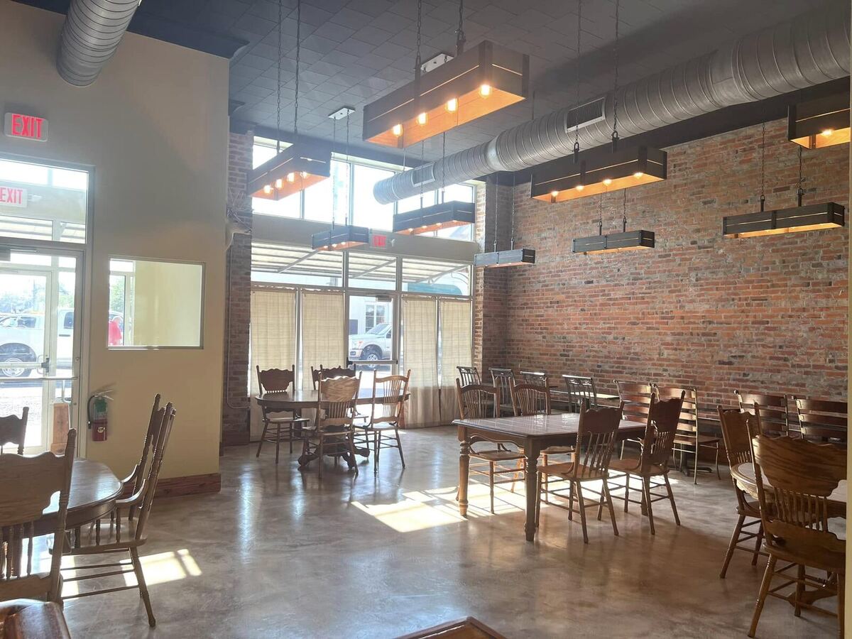 Sunlight pouring through tall storefront windows onto wood tables and an exposed brick wall inside The Russo.