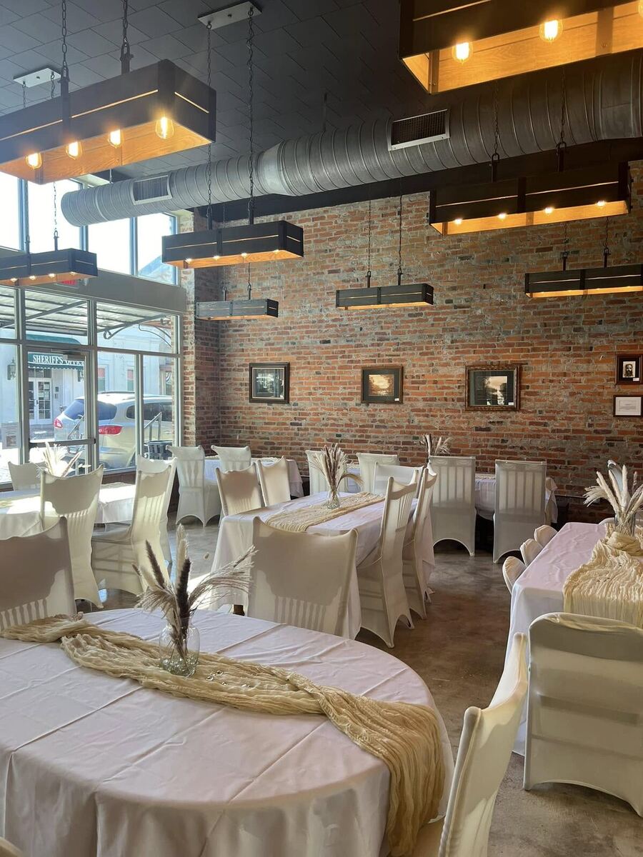 The Russo dressed for a celebration with ivory linens, draped table runners, and pampas grass centerpieces against the brick wall.