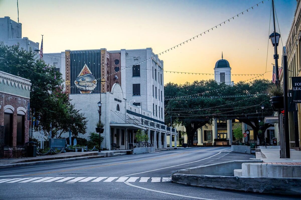 Historic downtown Abbeville at dusk — string lights over the street, oak trees, and the courthouse cupola against the evening sky.