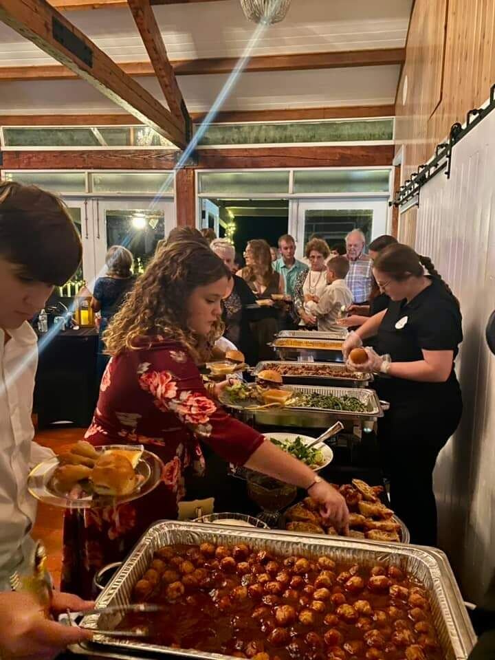 Guests serving themselves down a Southern Spread buffet line of chafing dishes, including saucy meatballs and sliders, with staff assisting.
