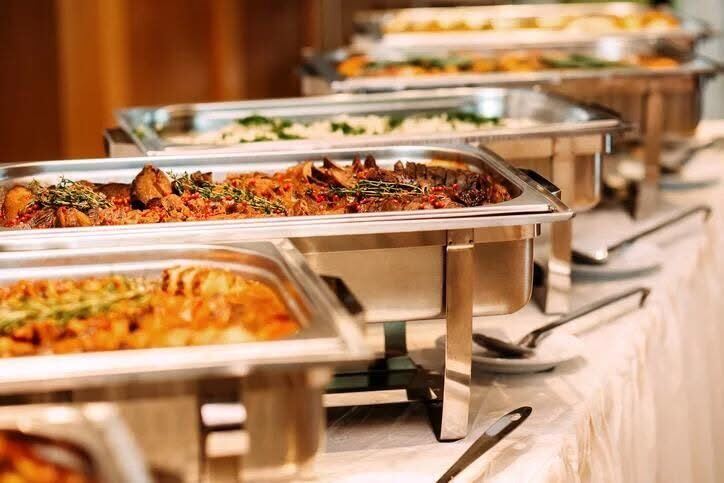 A catering buffet line of chafing dishes filled with roasted meats, rice, and vegetables, ready to serve.