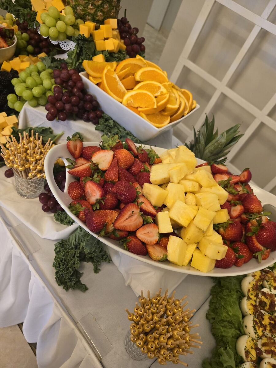 A fruit and cheese display — a platter of fresh strawberries and pineapple with grapes, orange slices, and cubed cheddar.