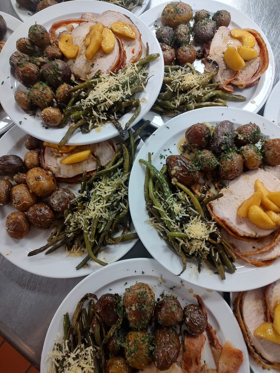 Plated dinners of sliced pork loin topped with glazed peaches, roasted baby potatoes, and parmesan green beans.